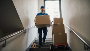 Professional movers carrying cardboard boxes up an urban apartment building staircase